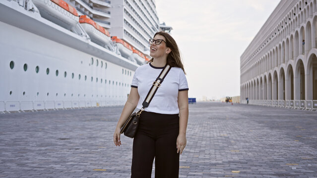 A smiling young woman in casual attire walks near a large cruise ship, signaling luxury sea travel.
