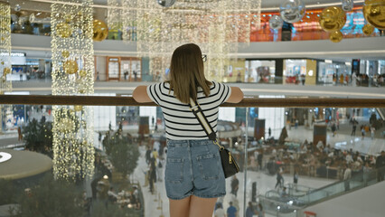 Back view of a brunette woman admiring a luxurious dubai mall's interior with hanging decorations.