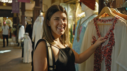 A smiling young woman shops for traditional clothing at a souk in dubai, exuding the charm of an arabian tourist destination.