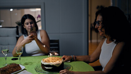Two women celebrate indoors with a cake featuring sparkling candles, capturing a casual, joyful...
