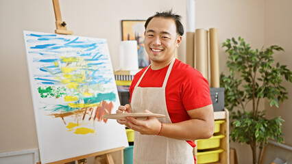 Smiling, confident young chinese man passionately draws in art studio, enjoying his artistic hobby