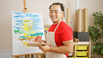 Smiling, confident young chinese man passionately draws in art studio, enjoying his artistic hobby