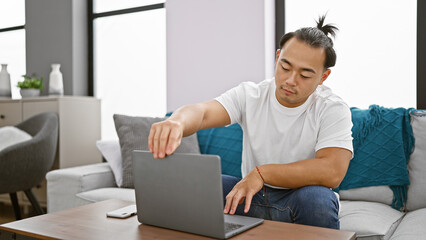 Handsome young chinese man, relaxed yet concentrated, opening his laptop while sitting on the sofa...