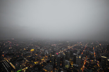 A thick fog appears over an overhead cityscape, giving off a dystopian futuristic atmosphere caused by bright lights and pollution