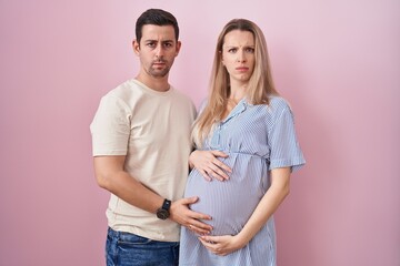 Fototapeta premium Young couple expecting a baby standing over pink background skeptic and nervous, frowning upset because of problem. negative person.