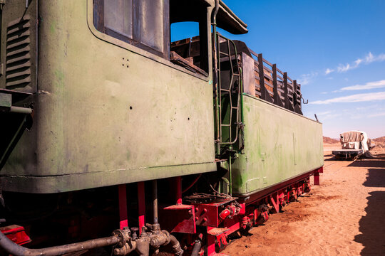 Close up detail of an old vintage steam train resting on the tracks in a wild and sunny desert environment with red wheels and green paint