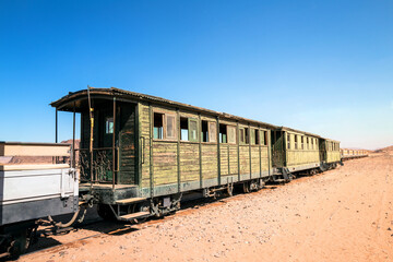 An old green wooden railcar from a bygone era rests on the tracks in a wild and sunny desert...