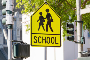 Yellow warning road sign for a school zone at a road intersection with a street traffic light in...