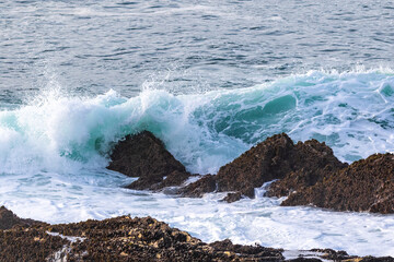 Wave breaking on rock, coast south of Morro Bay, California. Spray in the air; blue ocean in the background. 

