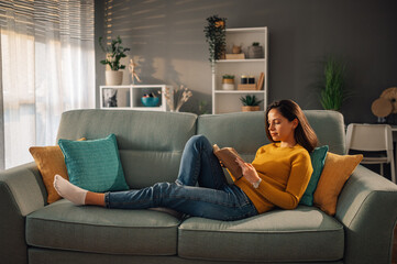 Woman relaxing and reading a book at home while lying on a sofa