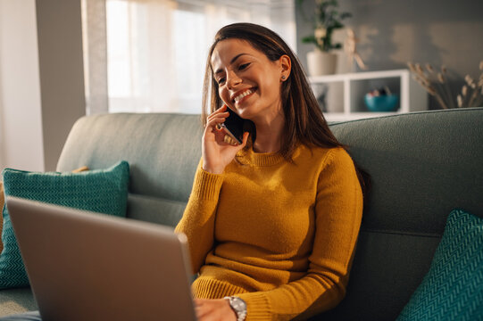 Woman talking with a client on the phone and using a laptop at home