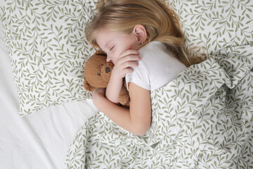 Sweet little girl sleeping in the bed and hugging her teddy bear	