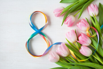 Number eight made from colored ribbon, pink tulips on a white wooden background. Postcard for International Women's Day March 8th.