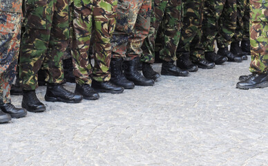 A row of legs and feet of British soldiers dressed in camouflage clothing and black leather army...