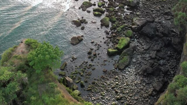 Aerial drone view of a coral cliff beach with rock, forest and calm waves. Taken place in Bali beach, tropical beach view.
