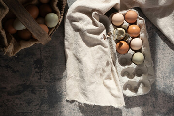 Fresh, heirloom eggs in an antique basket and a paper carton.  Sunlight making shadows from the...