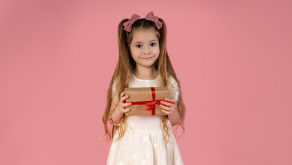 A little girl dressed in a prom dress with two very beautiful pigtails in her hair with two attractive pink bows. She is holding a gift she received for the holidays.