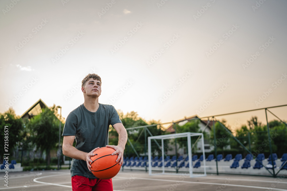 Wall mural One caucasian teenager stand on basketball court with ball