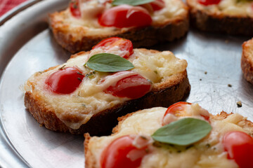 Photograph of cheese bruschetta with tomatoes and spices on a metal dish.