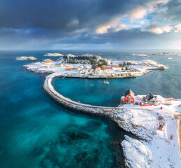 Aerial view of road and bridges, snowy rocks, islands with rorbu, sea, water, mountains, cloudy sky at sunset in winter. Beautiful north landscape. Top view of Henningsvaer, Lofoten islands, Norway