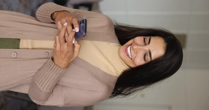 Smiling pretty female employee using smartphone indoors. Millennial woman share messages, communicates to client by e-mail, makes business call, ordering e-services, enjoy new business app