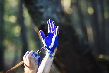 Artist painting her hand blue in the forest