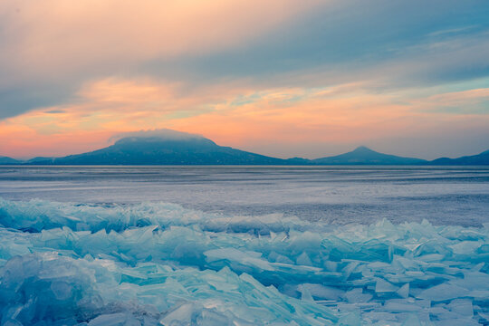 Fonyod, Hungary - Beautiful icebergs on the shore of the frozen Balaton. Badacsony and Gulacs with a spectacular cloudy sunset in the background. Winter landscape.