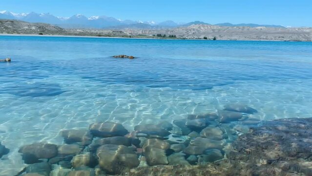 View of Issyk-Kul mountain lake, Kyrgyzstan. Waves splash on a sandy beach with rocks. Calm, peaceful natural background. Lake with a view of the Tien Shan Mountains. Kyrgyzstan 4K