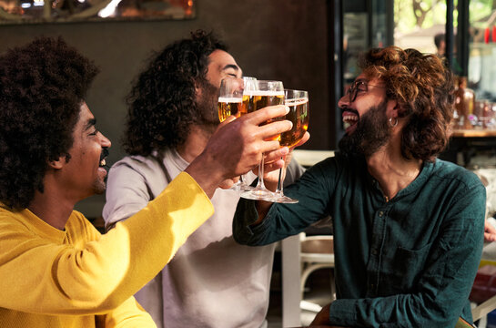 Happy multiethnic group of three men friends toasting with beers at a bar. Male people celebrating together. Copy space image.