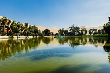 Fototapeta na wymiar Oasis of Huacachina near Ica city in Peru. Lake and trees inside the dunes. Travel destination in South American