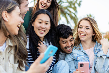 Group of young people using mobile phone sitting together having fun in an urban par. Young people, leisure and technology concept.