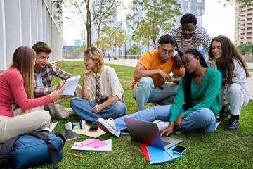 Group of young international university students sitting on the grass outside the faculty building....