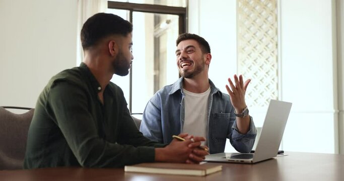 Male colleagues working on joint on-line presentation met in office using laptop, share ideas, consider task, mentor helps with program to new employee. Apprenticeship, teamwork, modern tech, workflow