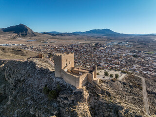 Obraz premium Aerial view of Jumilla medieval castle in Murcia Spain, on a hilltop, imposing irregular shape keep with four floors, crenelated battlements cloudy blue sky background