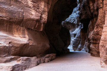 A sandstone canyon path moves between rocks with light breaking through in the distance. Rocks have rich texture from water erosion. No people with leading lines
