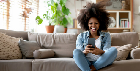 Excited happy young black woman holding smart phone device sitting on sofa at home - Happy satisfied female looking at mobile smartphone screen  - Technology concept - obrazy, fototapety, plakaty