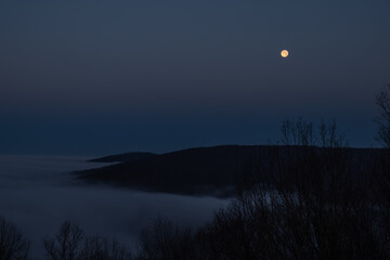 Twilight hour with the moon in view as seen from the bluffs of Sewanee, Tennessee as fog permeates...
