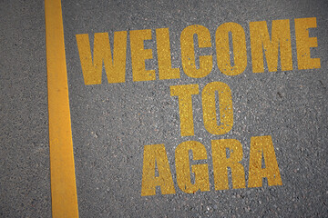 asphalt road with text welcome to Agra near yellow line.