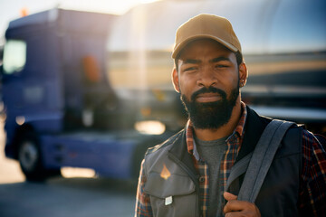 Black professional driver on truck parking lot looking at camera.