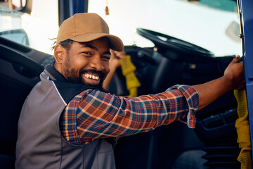 Happy black professional driver getting into truck and looking at camera. - obrazy, fototapety, plakaty