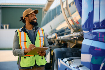 Happy black freight transportation dispatcher examining truck before ride.