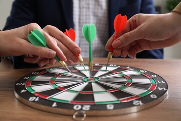 Business targeting concept. People with darts aiming at dartboard at table, closeup