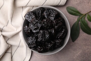 Sweet dried prunes in bowl on light brown table, top view