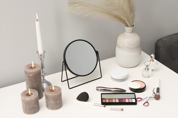 Dressing table with mirror, cosmetic products, perfumes and burning candles in makeup room