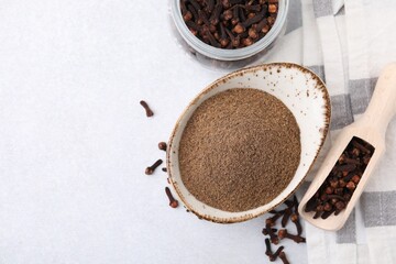 Aromatic clove powder, scoop and dried buds on light table, flat lay. Space for text