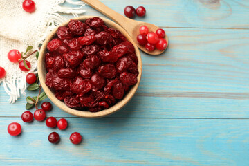 Tasty dried cranberries in bowl and fresh ones on light blue wooden table, top view. Space for text