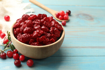 Tasty dried cranberries in bowl and fresh ones on light blue wooden table, closeup. Space for text