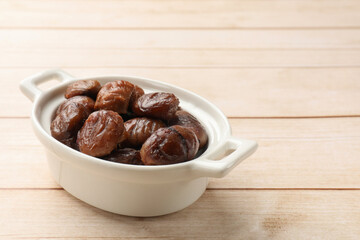 Roasted edible sweet chestnuts in dish on light wooden table, space for text