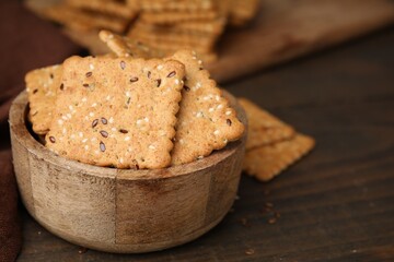 Cereal crackers with flax and sesame seeds in bowl on wooden table, closeup. Space for text