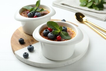 Delicious creme brulee with berries and mint in bowls on white wooden table, closeup